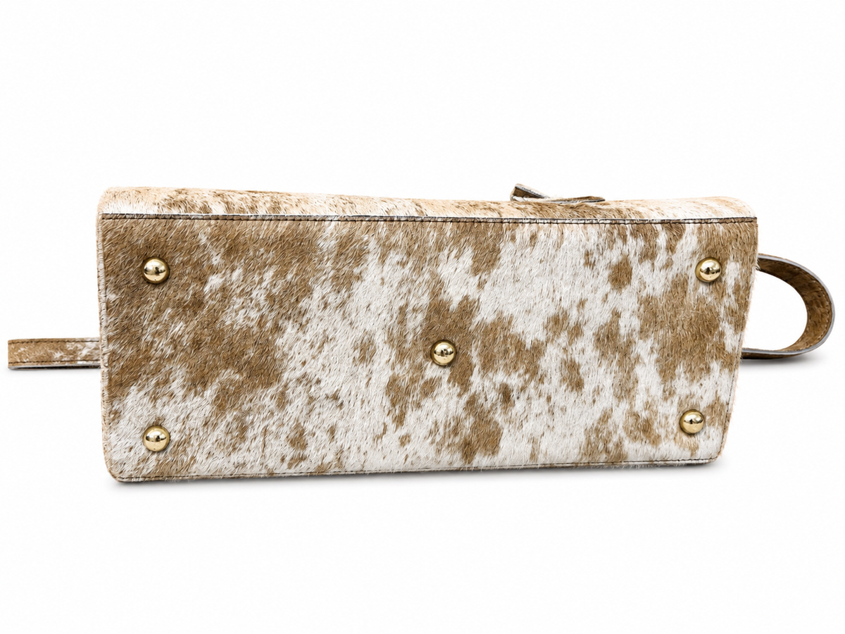 A rectangular clutch bag with a brown and white cowhide pattern, featuring gold-tone metal studs and a matching leather strap on a white background.