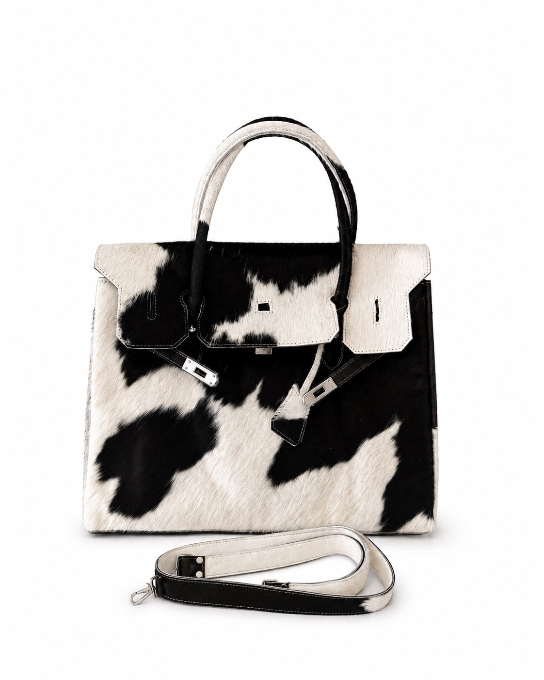 A structured handbag with a black and white cow print pattern, featuring dual top handles and a detachable shoulder strap, displayed on a clean white background.