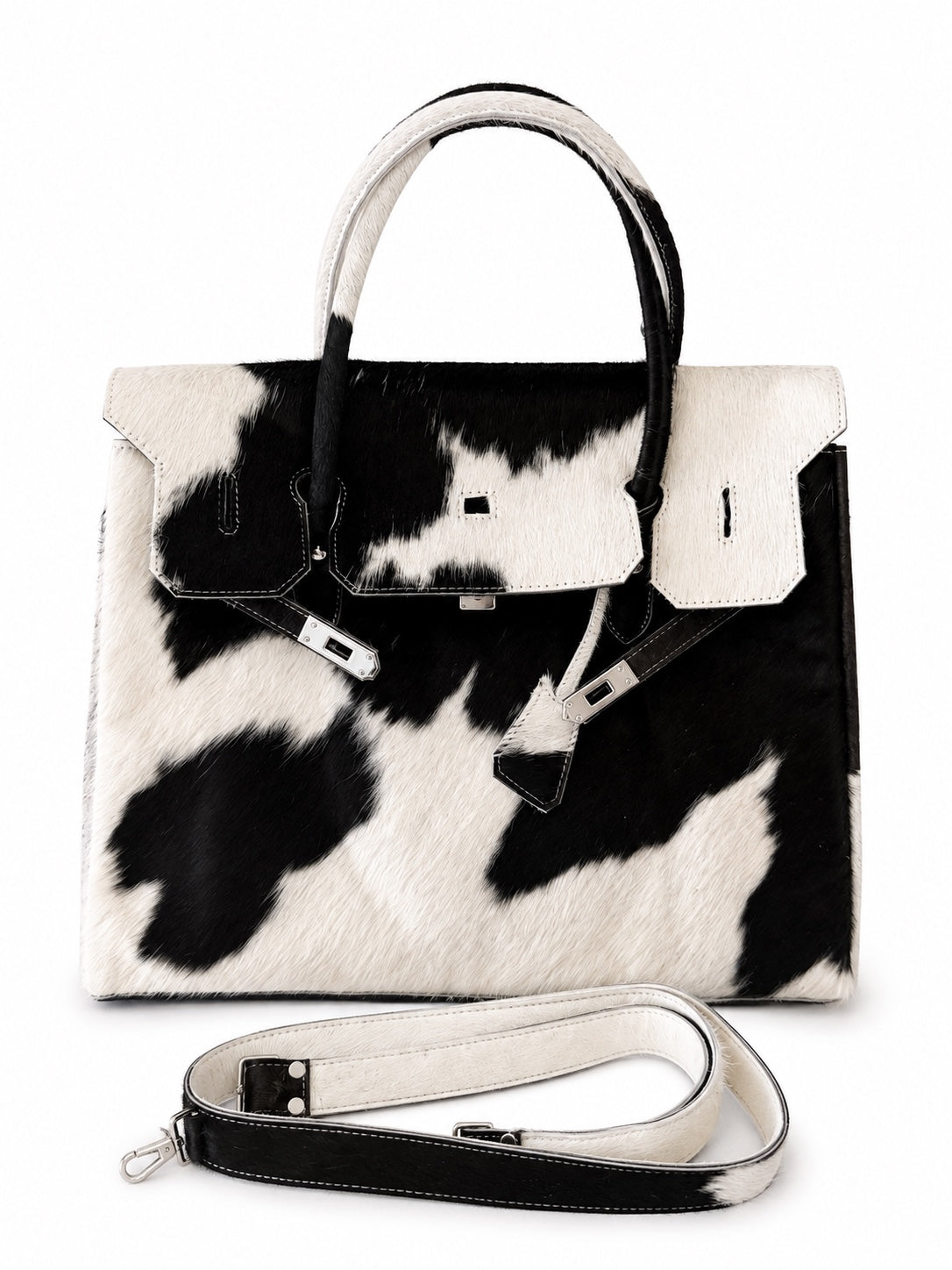 A structured handbag with a black and white cow print pattern, featuring dual top handles and a detachable shoulder strap, displayed on a clean white background.