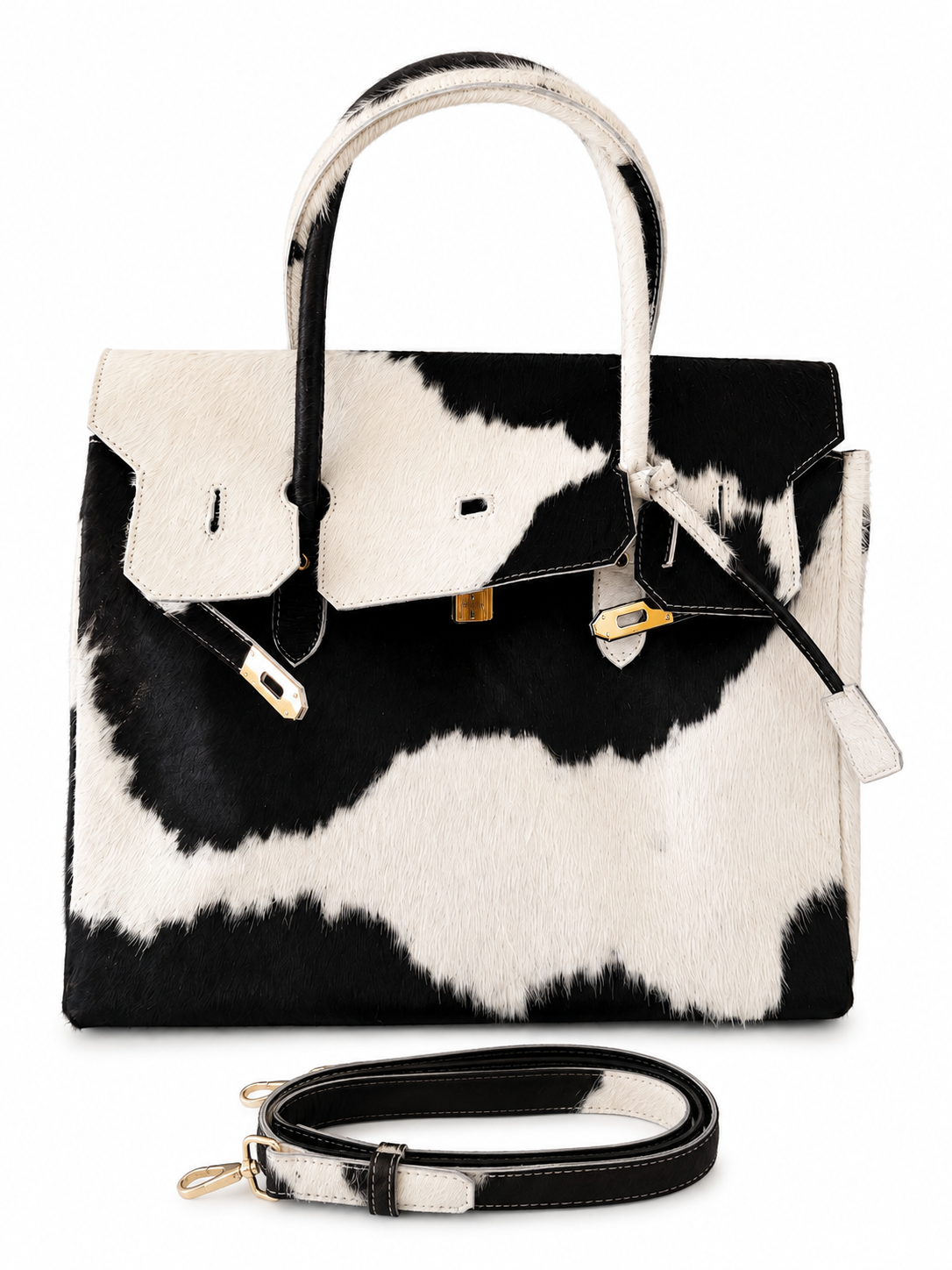 A structured handbag with a black and white cowhide pattern, featuring dual top handles, a front flap with gold-tone hardware, and a matching black and white cowhide shoulder strap displayed below on a white background.