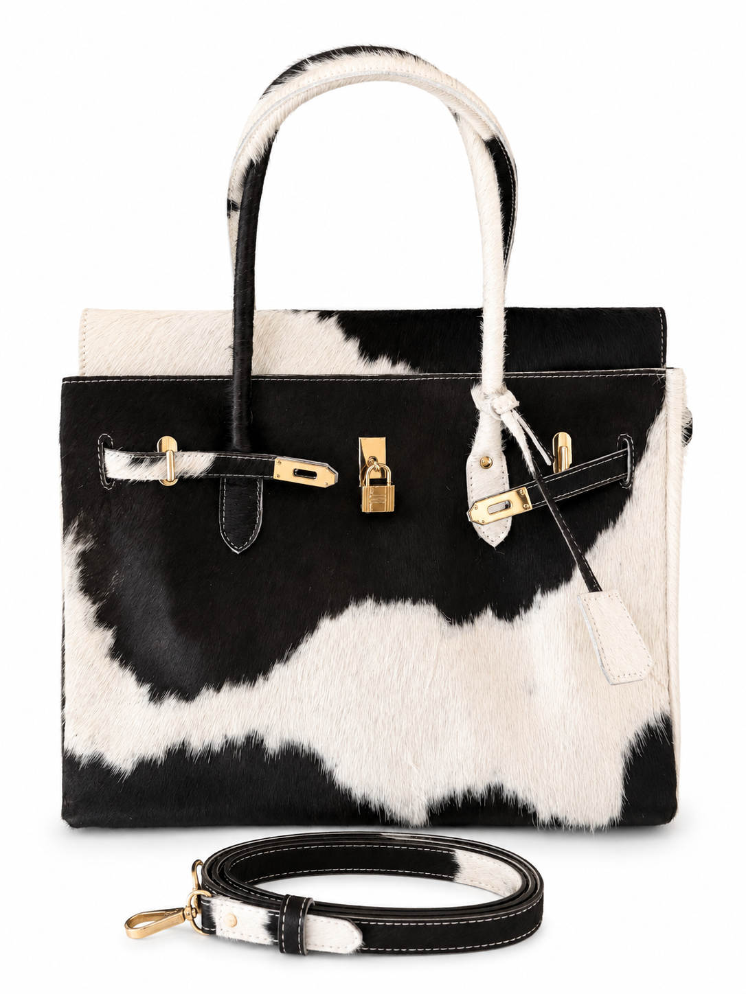 A structured handbag with a black and white cowhide pattern, featuring gold-tone hardware, dual top handles, and a matching detachable shoulder strap displayed in front on a white background.