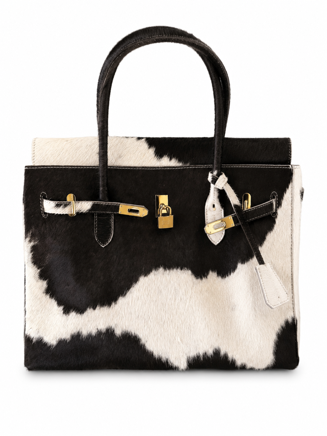 A structured handbag with a black and white cowhide pattern, featuring black leather handles, gold-tone hardware, and a white leather clochette on a plain white background.