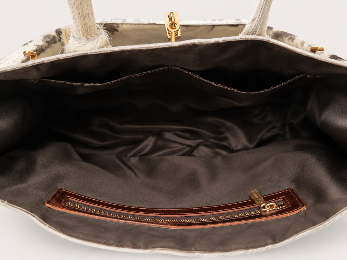 Close-up of the interior of a handbag, showing a dark brown satin-lined compartment with a brown leather zipper pocket and gold-tone hardware.