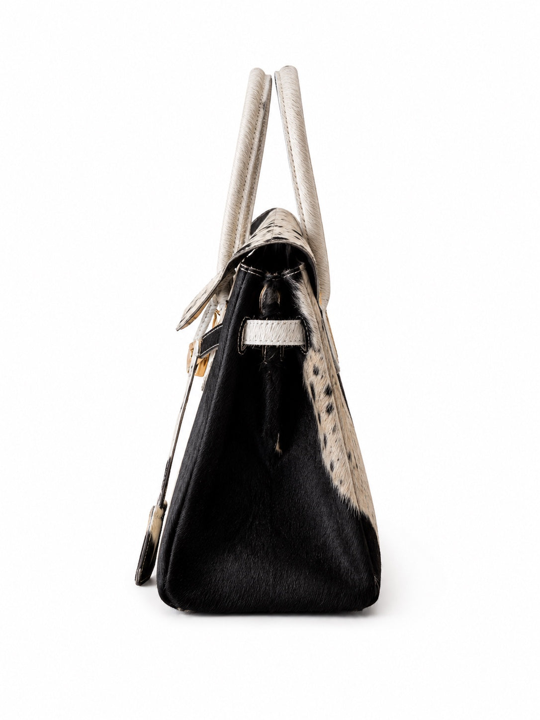 A structured handbag with a black and white cowhide pattern, featuring cream-colored handles and trim, photographed against a solid white background.