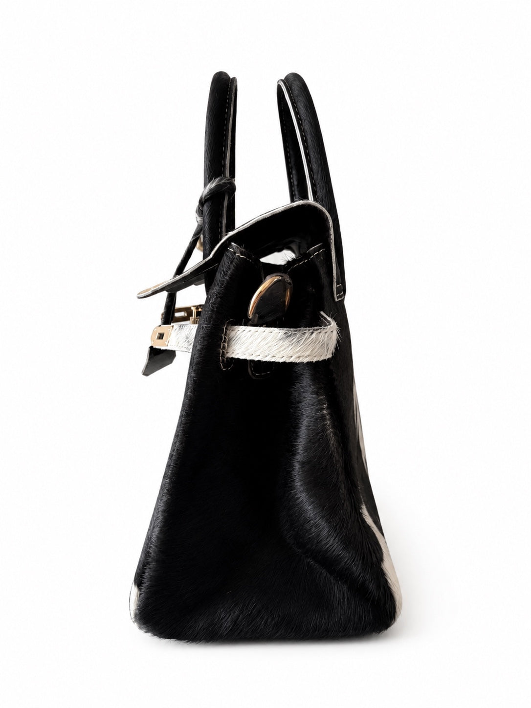 A black hair-on-hide handbag with a textured white strap and gold-tone hardware, shown from a side profile view on a white background.