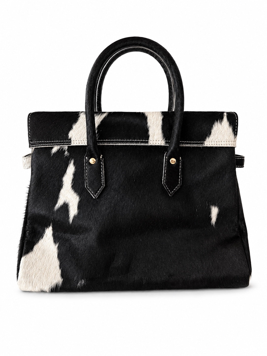 A structured handbag with a black and white cowhide pattern, black leather handles, and gold-tone hardware, shown against a plain white background.