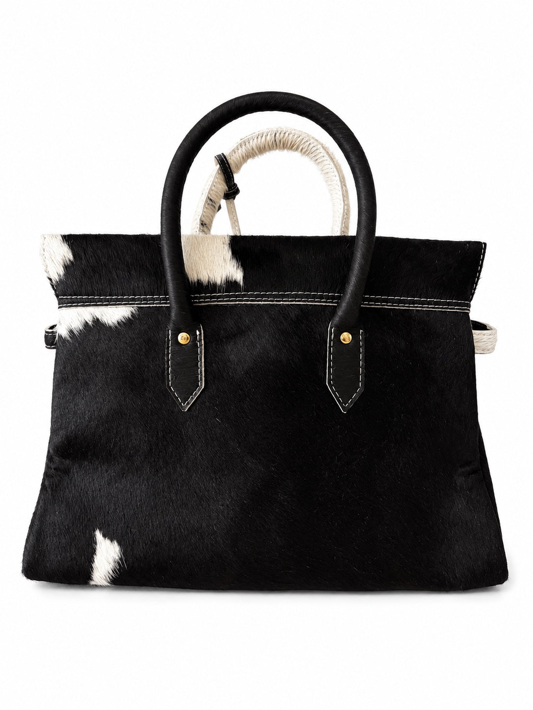 A black and white cowhide handbag with black leather handles and gold-tone hardware, shown against a plain white background.
