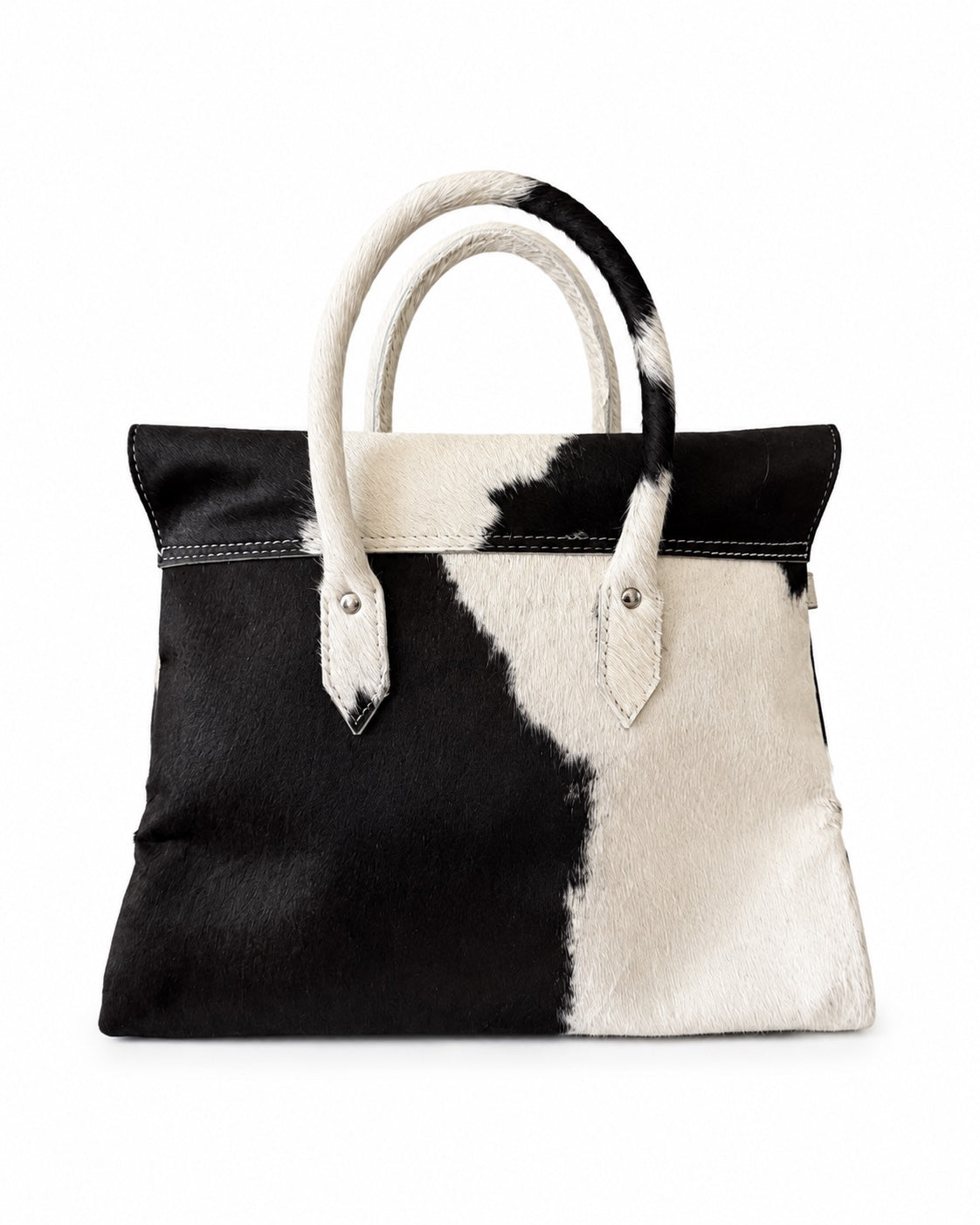 A black and white cowhide handbag with dual top handles, photographed against a solid white background.