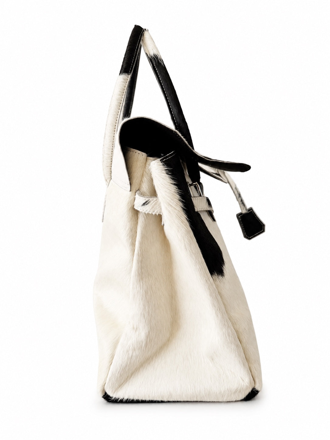 A white cowhide tote bag with black leather trim and handles, shown from a side profile view against a white background.