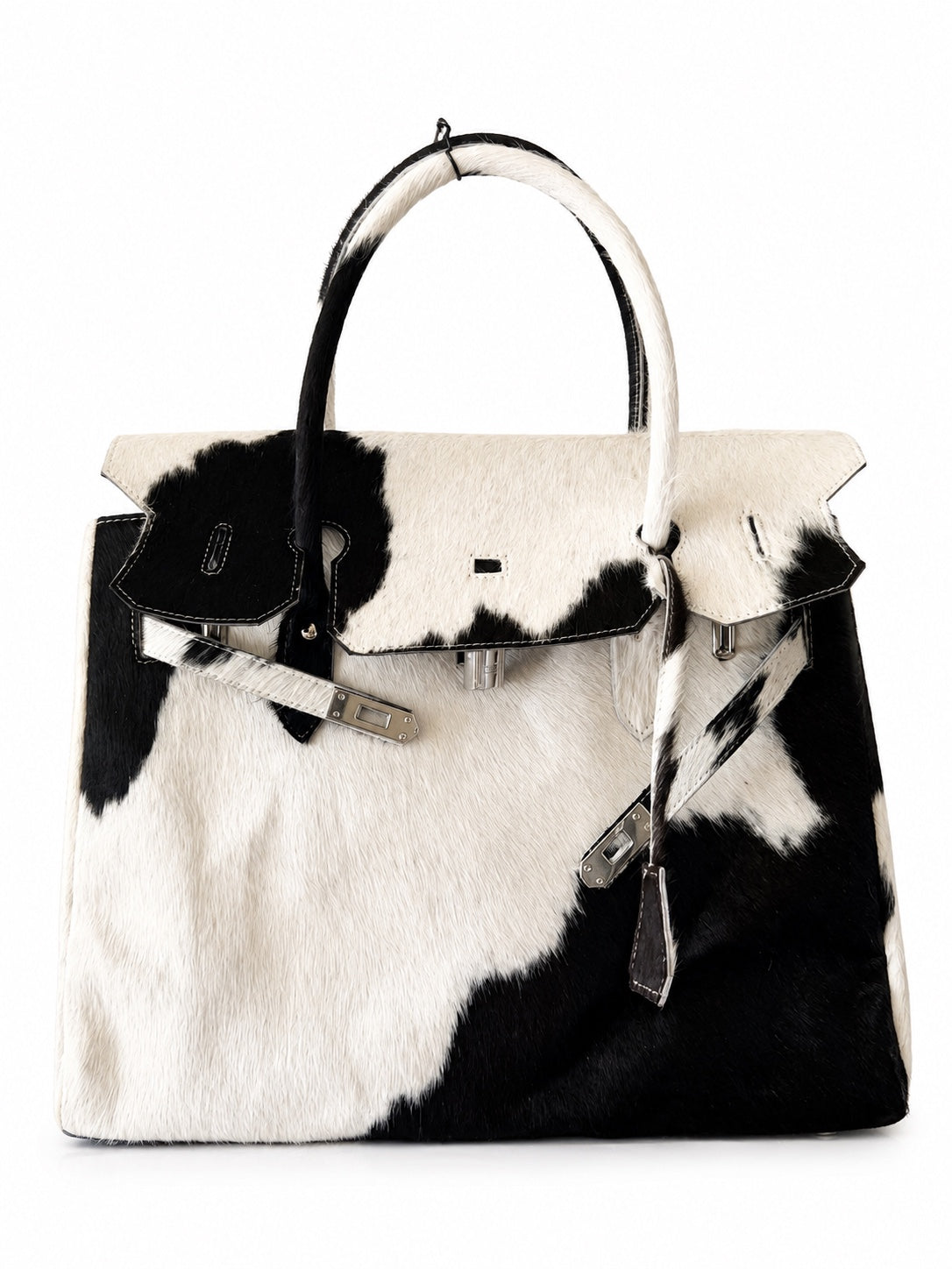 A structured handbag with a black and white cowhide pattern, featuring silver-tone hardware, a top handle, and a front flap closure, photographed against a plain white background.
