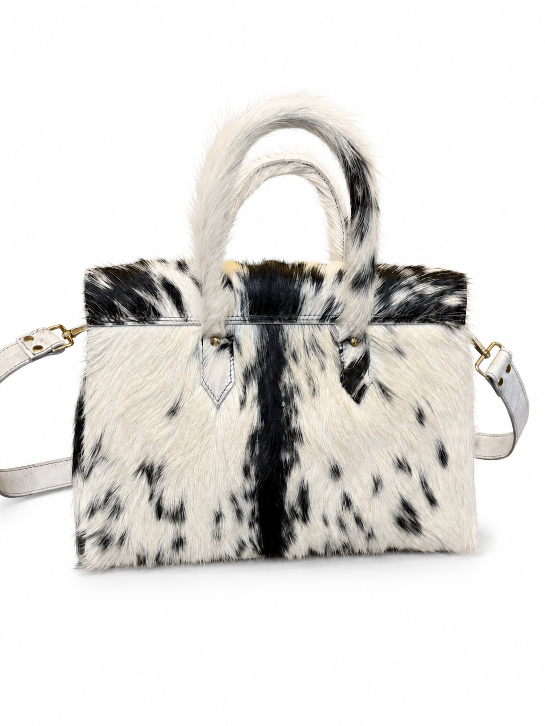A cowhide handbag with black and white spotted pattern, featuring dual top handles, a top handle loop, and a shoulder strap on a white background.