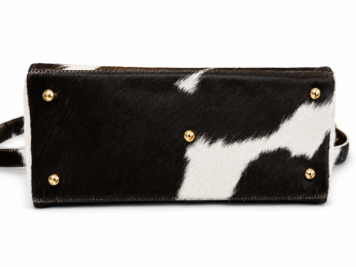 A black and white cowhide clutch bag with gold-tone metal studs, shown from the front on a white background.