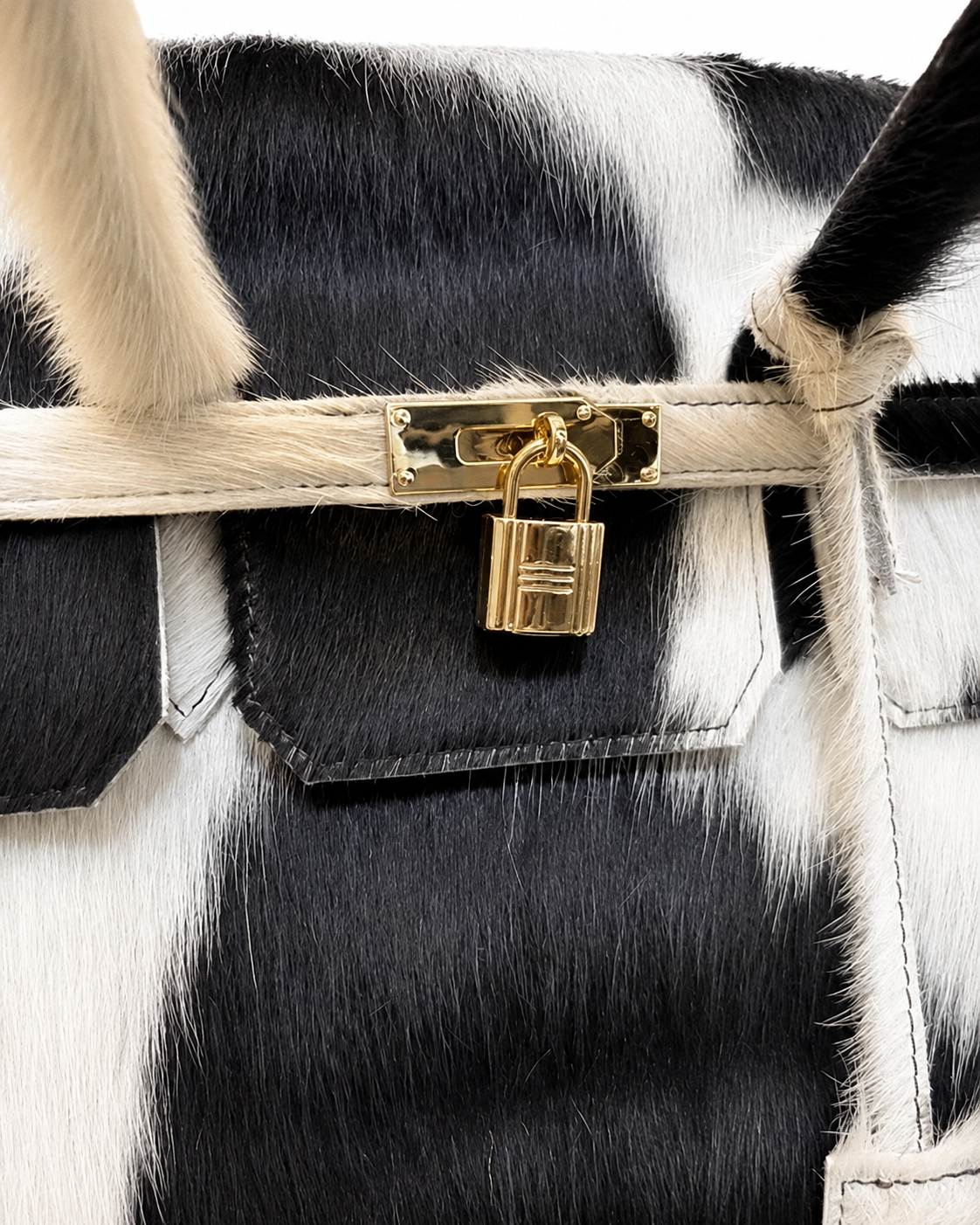 Close-up of a black and white cowhide handbag with a gold padlock and strap closure.
