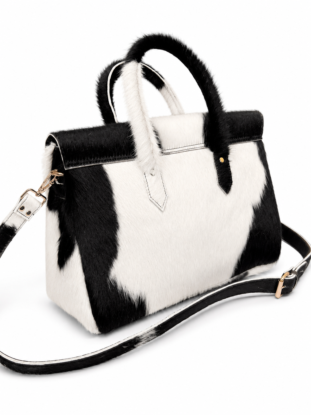 A black and white cow-print handbag with faux fur trim on the handles and a matching black and white shoulder strap, shown on a white background.